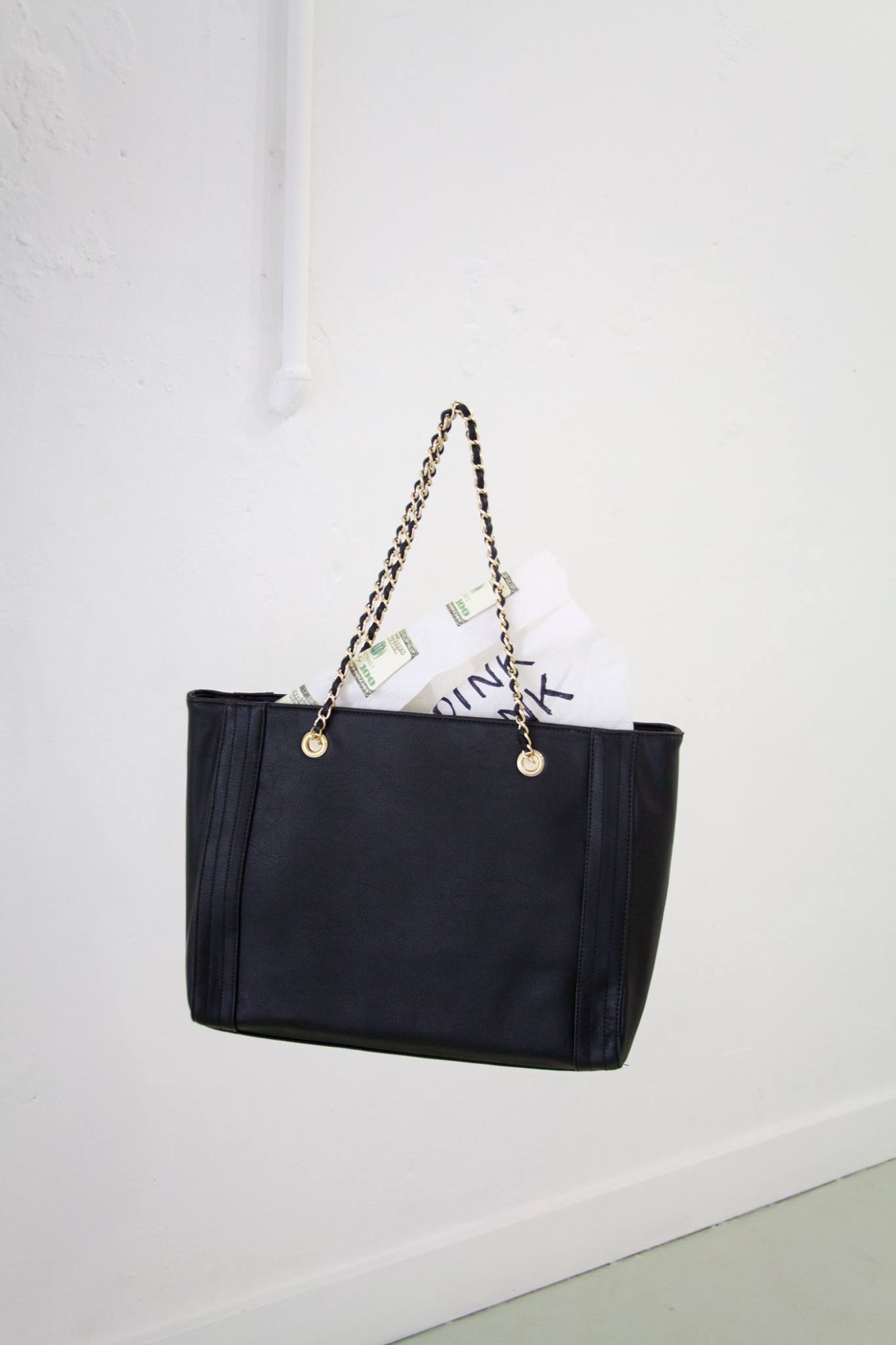 A floating black purse full of paper towels with money on it in a room with white walls